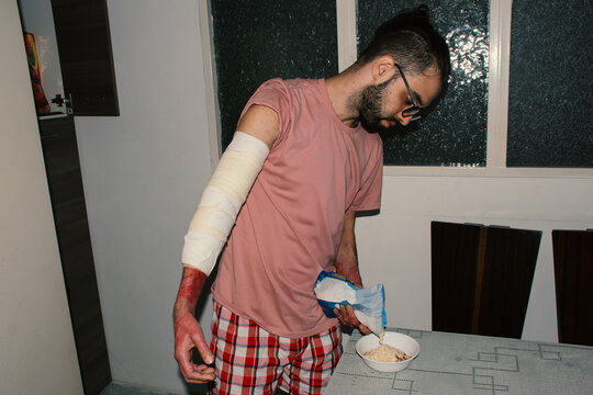 Man with bandaged arm prepares meal at home during evening