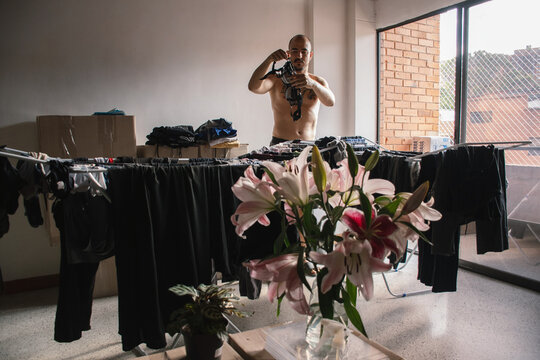 Man hangs clothes indoors while surrounded by flowers and boxes