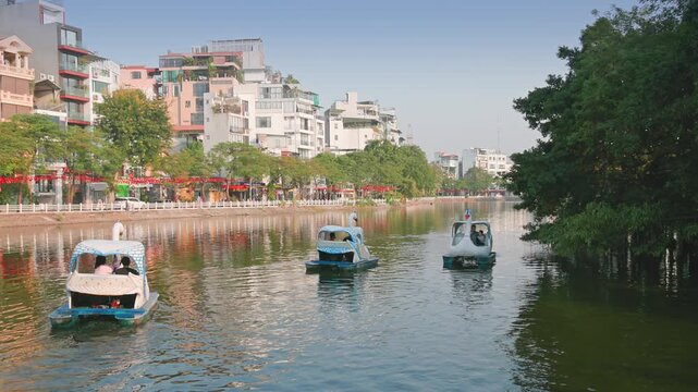 People enjoy swan paddle boats on the serene Tr&uacute;c Bạch Lake in Hanoi, Vietnam. Tourists and locals alike enjoy the recreational activity on a sunny day in Southeast Asia.