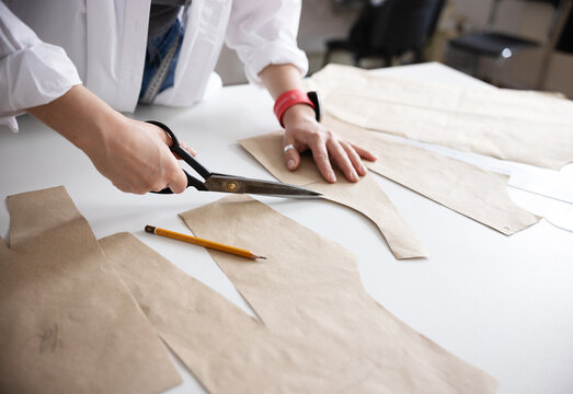 A close-up of a hands cutting paper patterns on a white table.