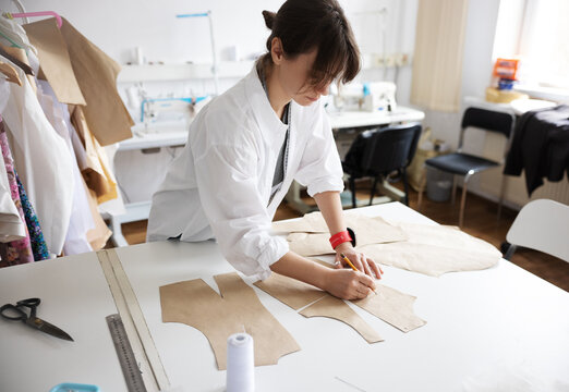 A young woman making clothing patterns in atelier.