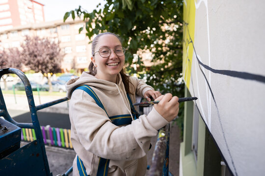 Smiling female painter using a lift is painting a large mural