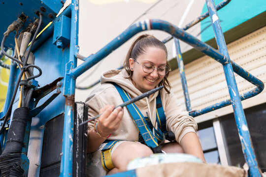 Female artist painting a mural with a brush on a lift platform