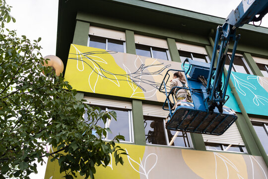 Woman artist painting large mural on building facade using aerial
