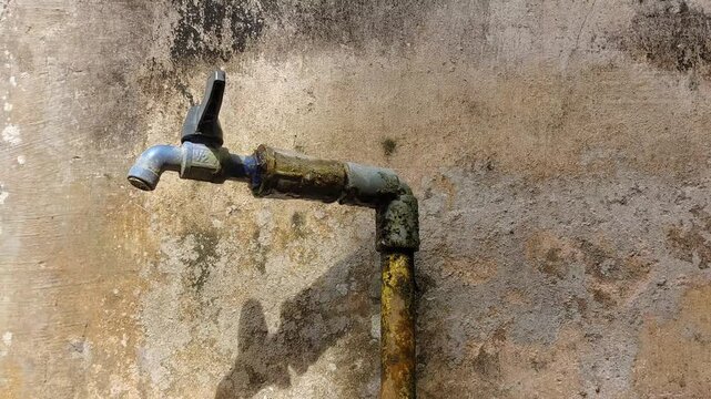 Close up cinematic video of an old outdoor water faucet covered in dirt and moss, mounted beside a house with a worn and weathered wall in the background. 
