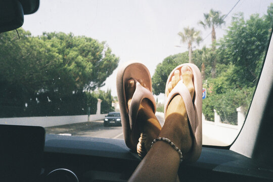 Feet with flip-flops on car dashboard
