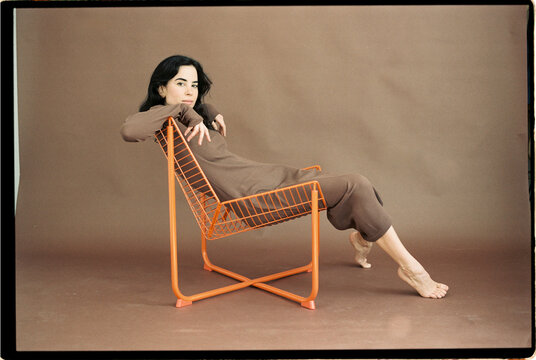 Woman sitting sideways on orange wire chair