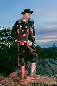 Man&rsquo;s silhouette in a cowboy suit and hat stands at sunset back behind