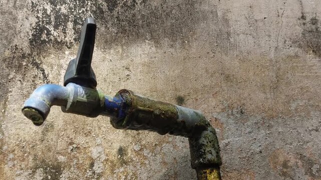 Close up cinematic video of an old outdoor water faucet covered in dirt and moss, mounted beside a house with a worn and weathered wall in the background. 