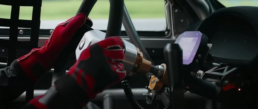 Racing driver shifting gears with red gloves on steering wheel