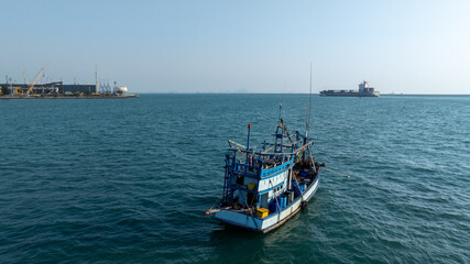 Obraz premium Traditional wooden Thai fishing boat with massive industrial and cargo terminal, Contrast and coexistence between local livelihoods and growth modern heavy industry.