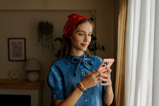 Woman using smartphone near window at home