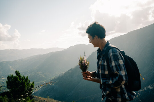 Person With Backpack Exploring Mountains and Holding Flowers