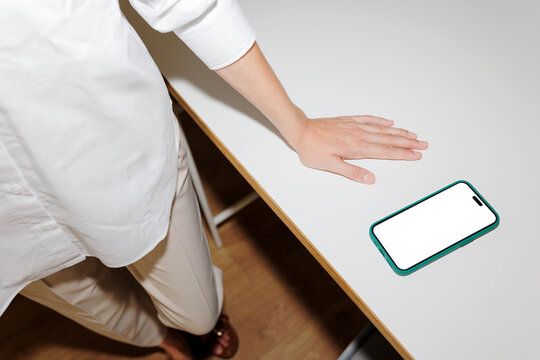 Manager leaning on desk with smartphone showing blank screen