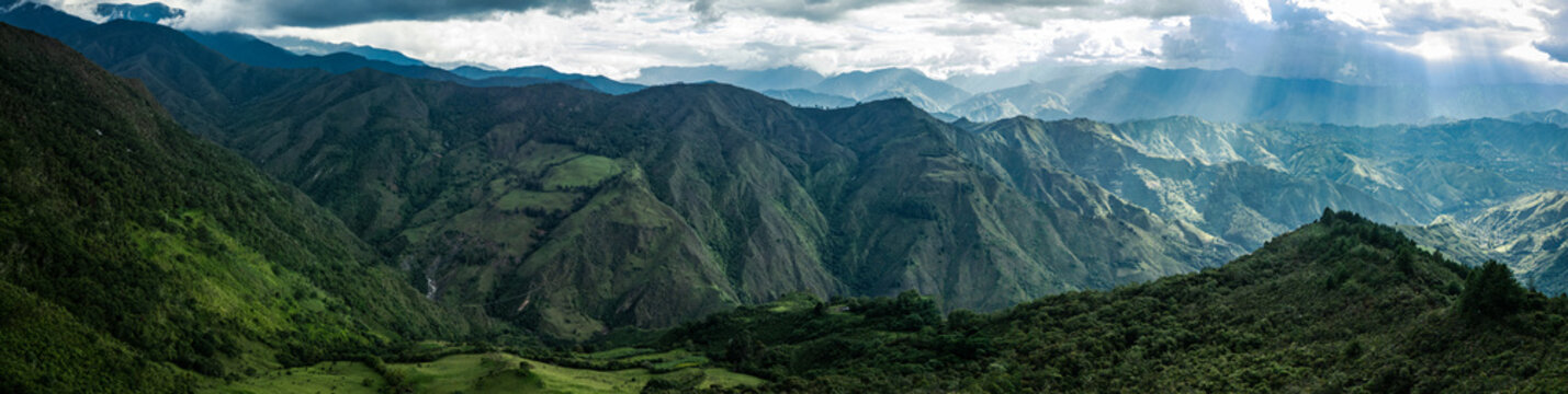 Dramatic aerial drone view of the lush green Andean mountain valleys near Vilcabamba, Loja Province, Ecuador, with spectacular god rays of sunlight breaking through dramatic clouds, illuminating the l