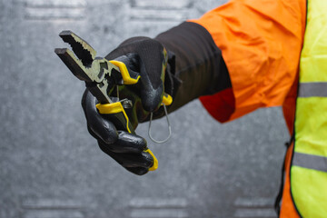 Construction worker wearing protective gloves and safety vest holding metal pliers. Concept of repair, maintenance and manual labor in construction and industrial work.