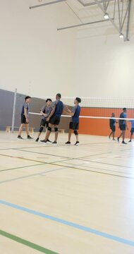 Vertical video: Diverse male teammates supporting player after dive on court, serving ball over net