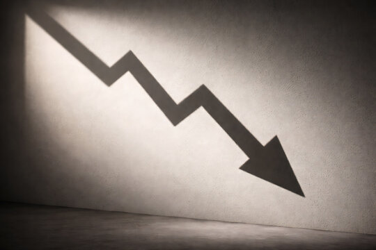 A downward arrow symbol casts a shadow on a textured wall, indicating decline or decrease. The shadows create a sense of depth and contrast, emphasizing the direction of the arrow.