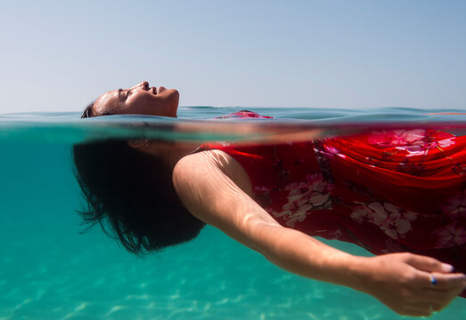 Cheerful woman floating in the sea with red dress