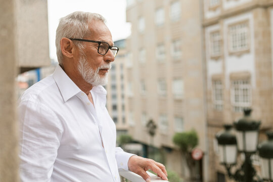 Older Man Gazing Thoughtfully From Balcony in Urban Setting