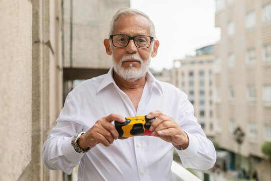 Senior Man Holding a Camera on a Balcony in an Urban Setting