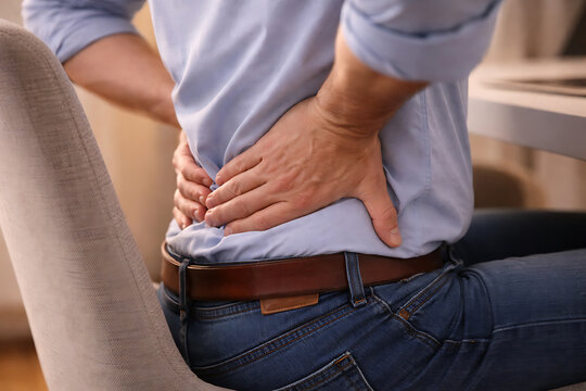 A man, experiencing pain, clutching his lower back, highlighting a health concern