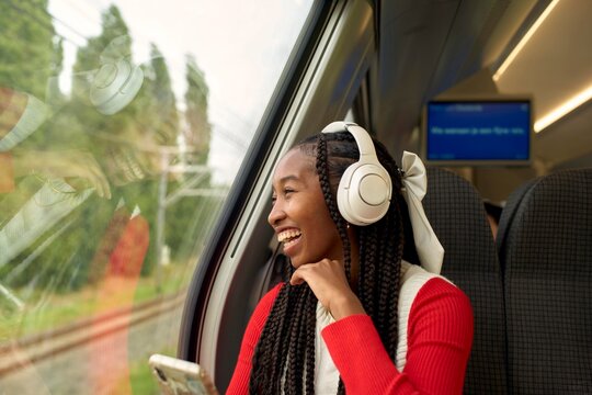 Smiling Woman Listens to Music on Train While Enjoying the View
