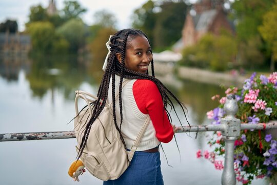 Young Woman With Braids Smiles by the River in a Charming Location