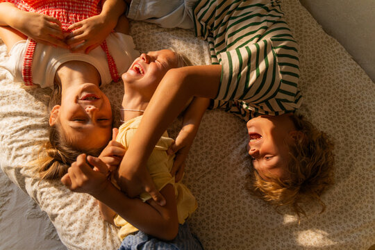 Three kids are messing around lying on the bed