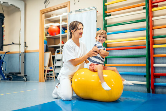 Physiotherapist assisting child with peanut ball balance exercises