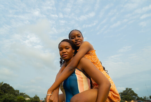 Young African Woman Carrying Her Sister on Her Back Outdoors.