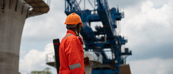 The survey team is operating a theodolite while referencing road construction plans. Civil engineers are taking measurements with surveying equipment at the construction site.