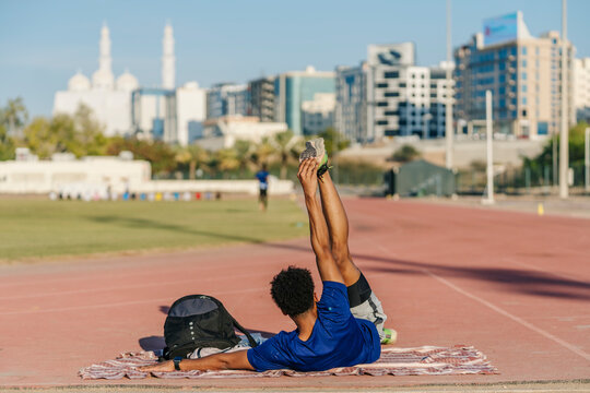 Young athlete stretching legs on running track in Muscat, Oman