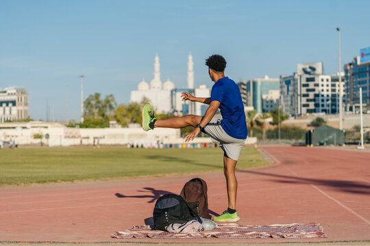 Young athlete stretching leg on running track in Muscat, Oman