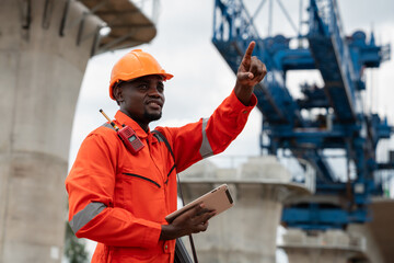The survey team is operating a theodolite while referencing road construction plans. Civil engineers are taking measurements with surveying equipment at the construction site.