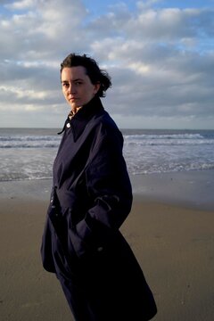 A Woman Poses Confidently on a Sandy Beach, Wearing a Dark Coat
