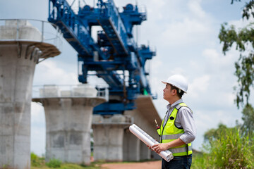 The survey team is operating a theodolite while referencing road construction plans. Civil engineers are taking measurements with surveying equipment at the construction site.