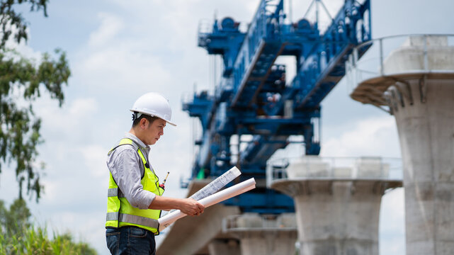 The survey team is operating a theodolite while referencing road construction plans. Civil engineers are taking measurements with surveying equipment at the construction site.