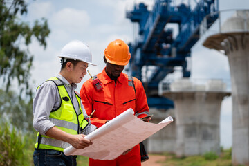 The survey team is operating a theodolite while referencing road construction plans. Civil engineers are taking measurements with surveying equipment at the construction site.
