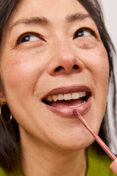 Beautiful asian woman applying brown lipstick