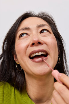 Beautiful asian woman applying brown lipstick