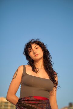 Woman With Curly Hair Standing Outdoors Under Clear Blue Sky