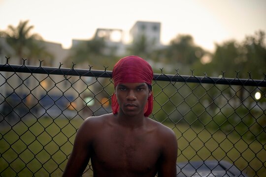 Young Man Wearing a Red Head Wrap Stands Near a Chain Link Fence