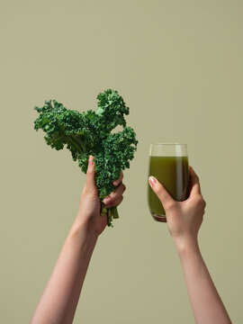A person holding kale and a glass of fresh and green juice