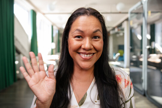 Smiling woman waving in office setting with a cheerful expression