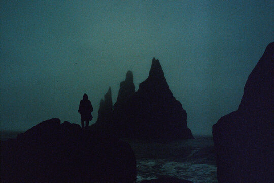 Silhouette of person near sea stacks in misty twilight