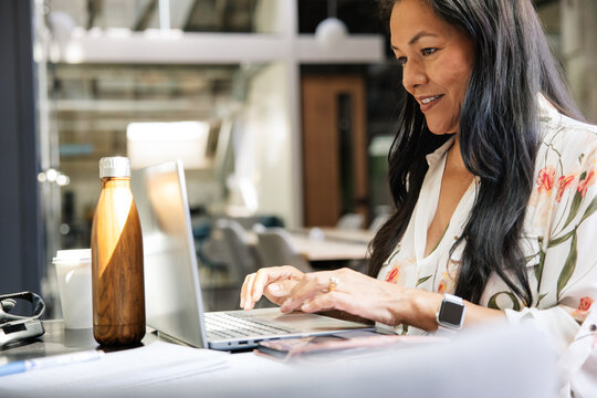Woman working on a laptop in an office with a bottle nearby