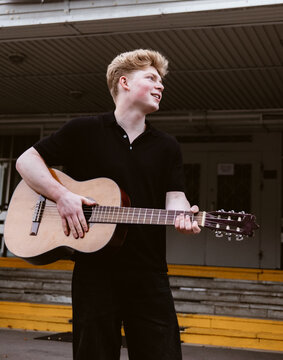 Young man playing guitar outdoors near school