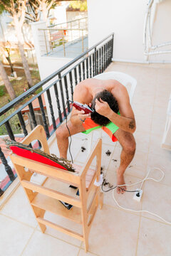Young man clipping his hair at the balcony