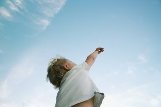 Child reaches up to the clear blue sky in a sunny outdoor setting